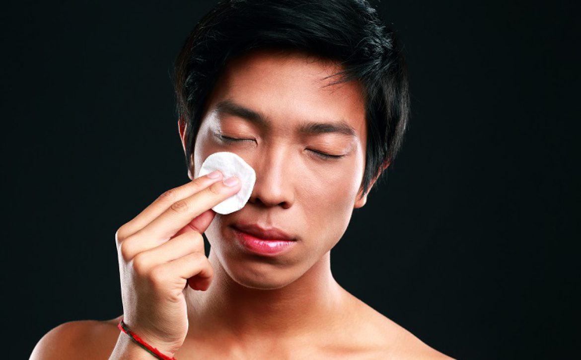 Asian man wipes his face with cotton pad on black background