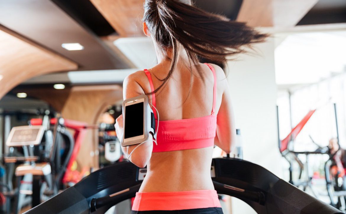 Woman athlete with balnk screen smartphone running on treadmill